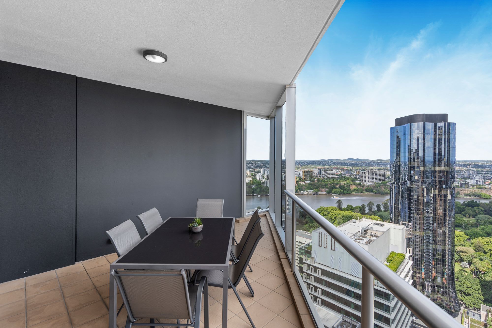 A balcony with a table and chairs, a potted plant, and a view of a cityscape and river.