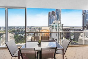 Een balkon met een glazen tafel en stoelen, met uitzicht op een stadsgezicht met moderne gebouwen en een heldere lucht.