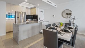 A modern kitchen with stainless steel appliances, a dining area with a white table set for four, and a round mirror on the wall. - City Skyline from Level 37 | Free Parking, Pool & Gym (Brisbane City)