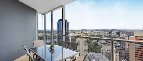 A balcony with a glass table and chairs, overlooking a cityscape with modern buildings.