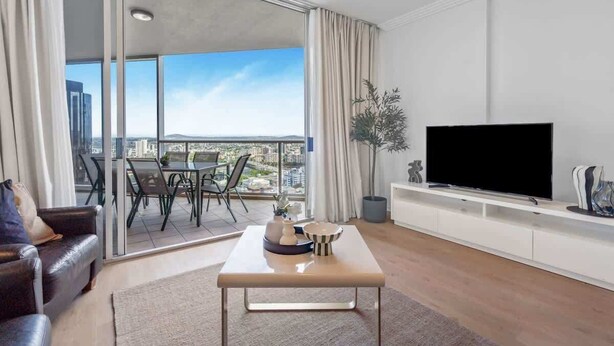 A modern living room with a flat-screen TV, a sofa, a coffee table, and a dining area with chairs. - City Skyline from Level 37 | Free Parking, Pool & Gym (Brisbane City)