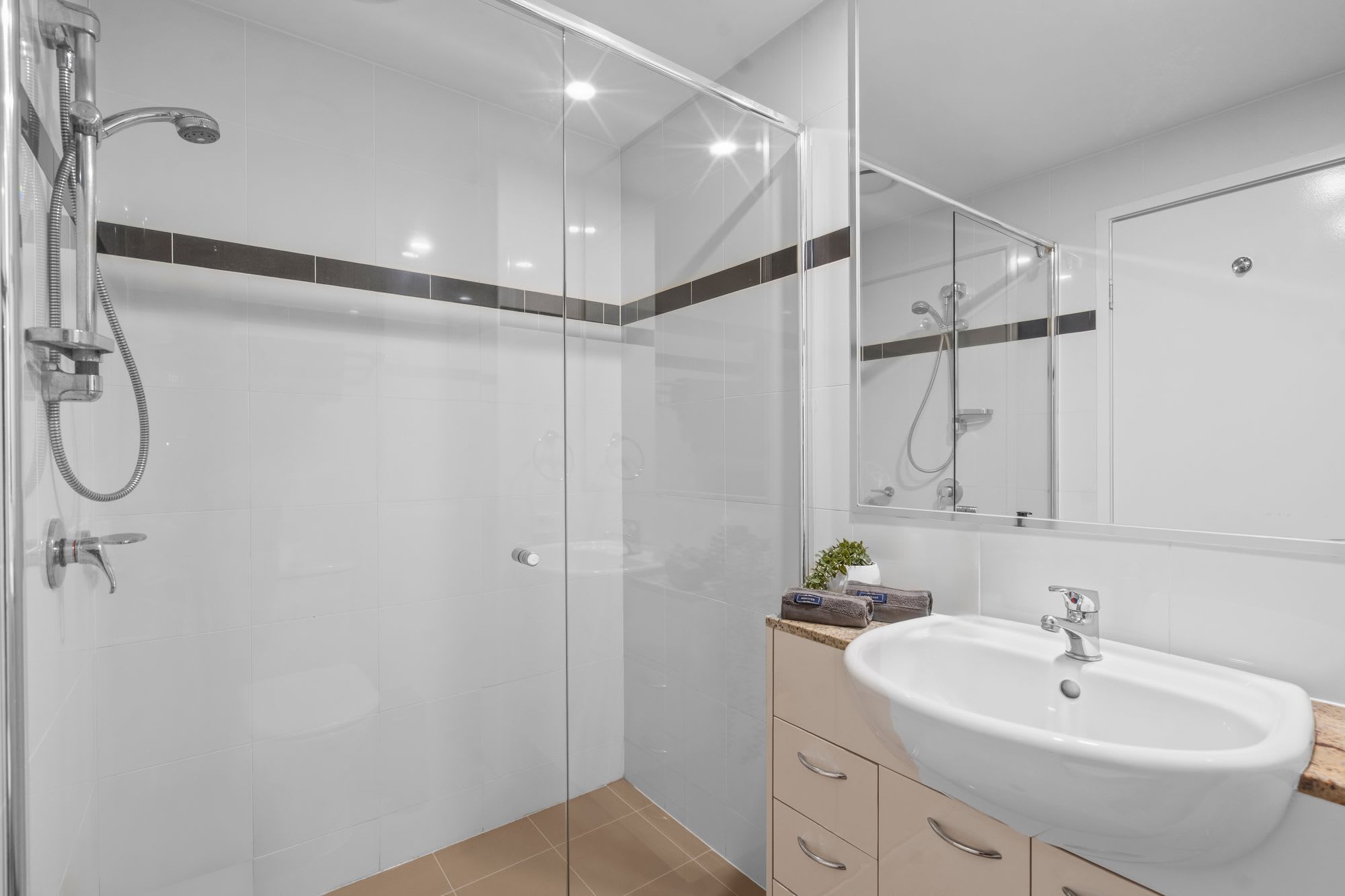 A modern bathroom with a glass-enclosed shower, a white sink, and a mirror.