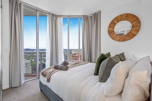 Een slaapkamer met een groot bed, uitzicht op de stad door ramen van de vloer tot aan het plafond en een ronde spiegel aan de muur.