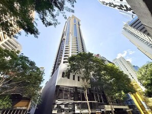 A tall, modern building with a reflective glass facade, surrounded by trees and other buildings. - City Skyline from Level 37 | Free Parking, Pool & Gym (Brisbane City)