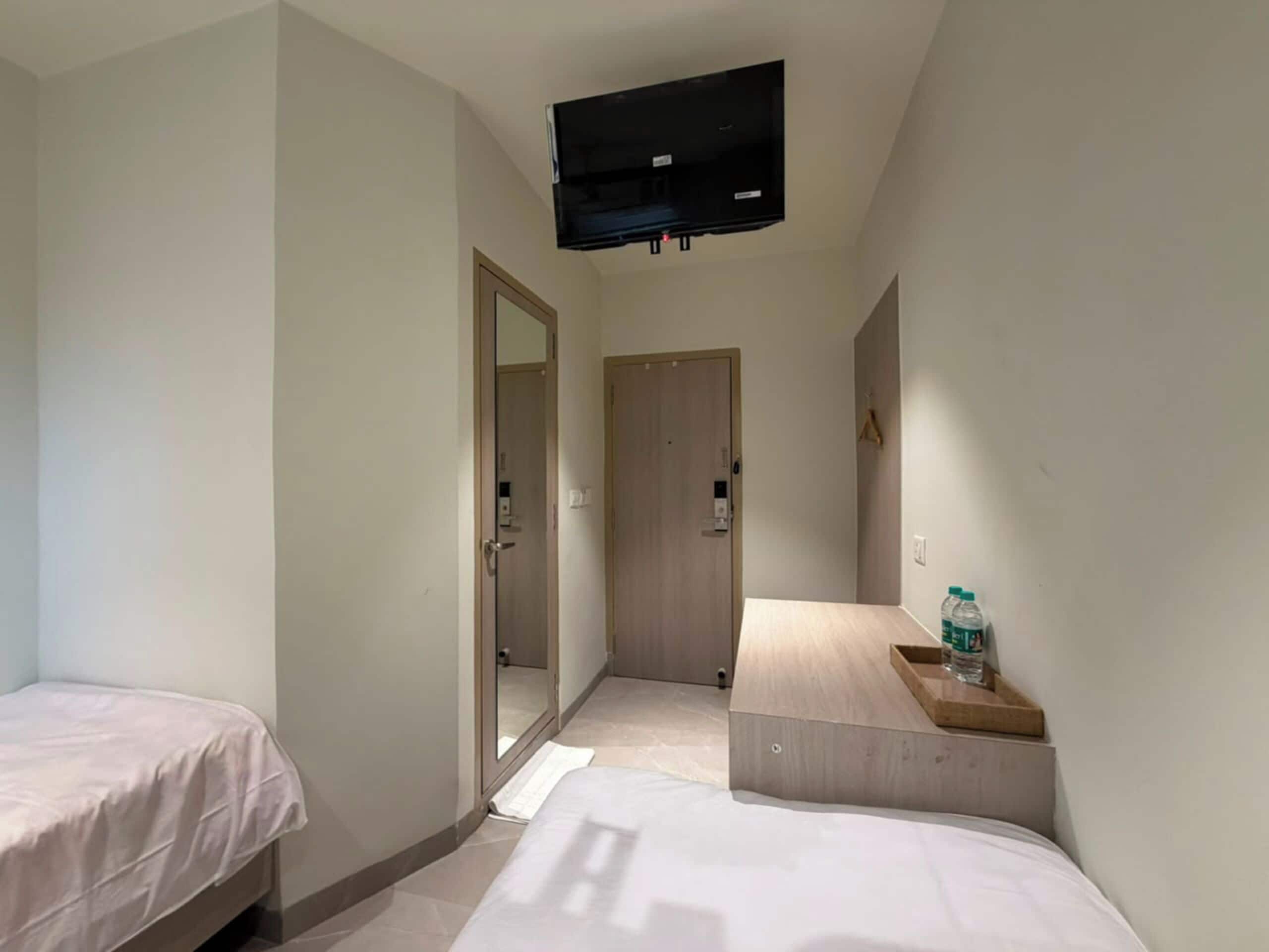 Een hotelkamer met twee enkele bedden, een wandgemonteerde flatscreen televisie en een tafeltje met een fles water.