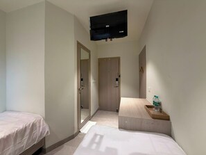 Habitación de hotel con dos camas individuales, un televisor de pantalla plana en la pared y una mesita con una botella de agua.
