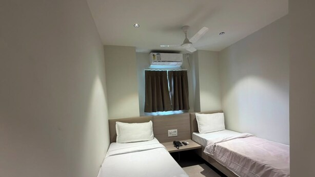 Una habitación de hotel con dos camas individuales, ventilador de techo, unidad de aire acondicionado y ventana con cortinas.