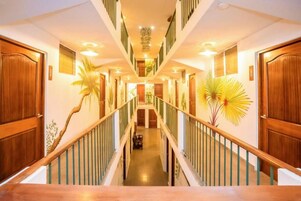 Un pasillo de hotel con puertas de madera, una escalera central y plantas en macetas.