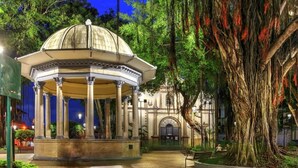 Un mirador con techo abovedado, rodeado de un jardín con un árbol grande.