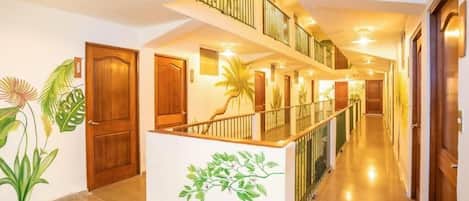 Pasillo de hotel con puertas de madera, un mostrador de recepción central blanco y una escalera que conduce a un nivel superior.