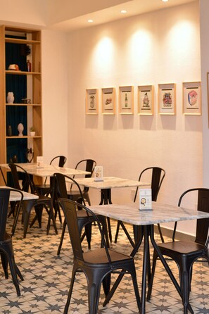 Un comedor con mesas y sillas, una pared decorada con cuadros, y una estantería con objetos decorativos.