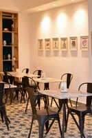 Un comedor con mesas y sillas, una pared decorada con cuadros, y una estantería con objetos decorativos.