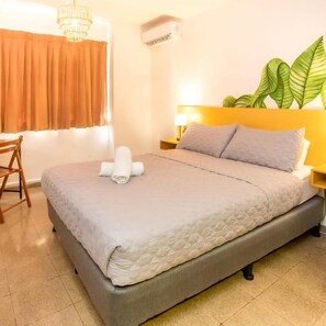 Una habitación de hotel con cama, escritorio, una silla, una planta y una araña.