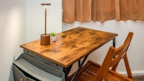 Una mesa de madera con una lámpara y una planta pequeña, una silla y un armario gris.
