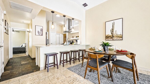 Een moderne keuken met een centraal eiland, barkrukken en een eettafel met stoelen.