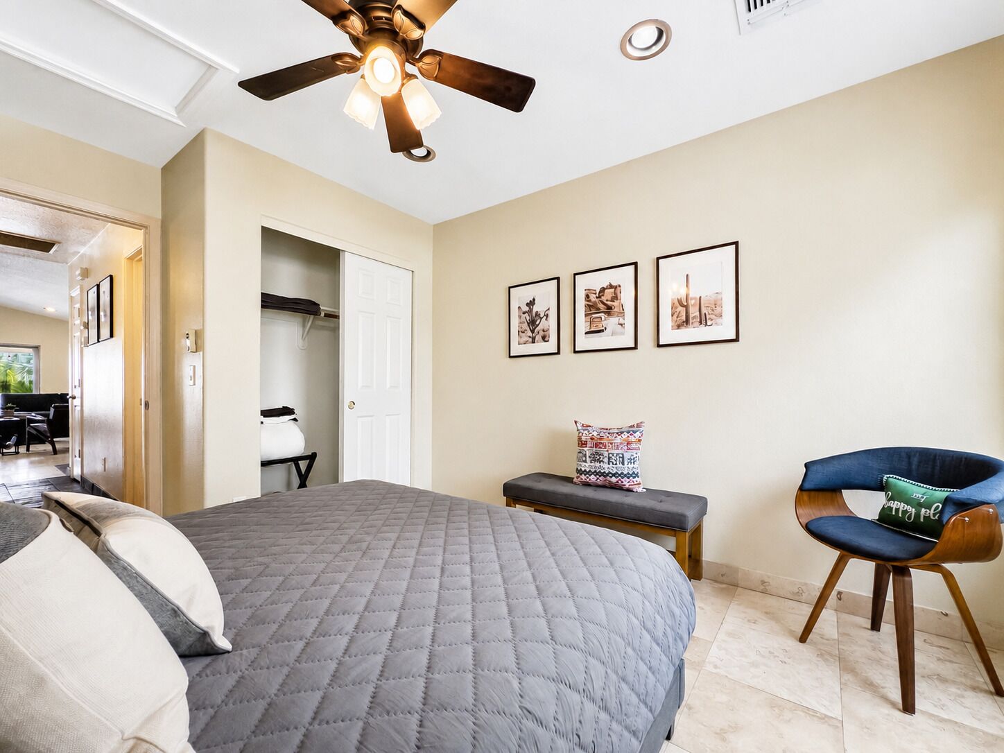 Une chambre à coucher avec un lit, un ventilateur de plafond, un banc, une chaise et des tableaux encadrés accrochés au mur.