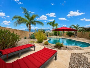 A backyard with a swimming pool, red lounge chairs, and a red umbrella. - 3BR w private pool, mountain views, gazebo (Oro Valley)