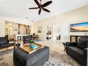 A modern living room with a ceiling fan, a dining area with a kitchen in the background, and a bedroom visible through an open door. - 3BR w private pool, mountain views, gazebo (Oro Valley)