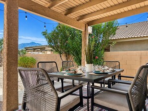 An outdoor patio with a table set for dining, surrounded by wicker chairs, under a wooden pergola. - 3BR w private pool, mountain views, gazebo (Oro Valley)
