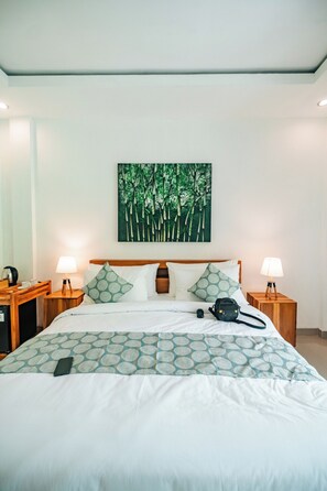 A neatly made bed with a patterned bedspread, two bedside tables with lamps, a wall-mounted painting of bamboo, and a wooden headboard. - Dteba Guest House (Tabanan)