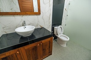 Un baño con lavamanos blanco, encimera negra, mueble de madera y un inodoro.