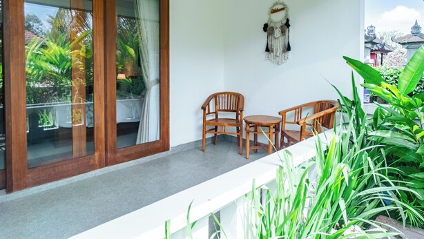 Un balcón con mesa y sillas de madera, un adorno colgante y abundante vegetación.