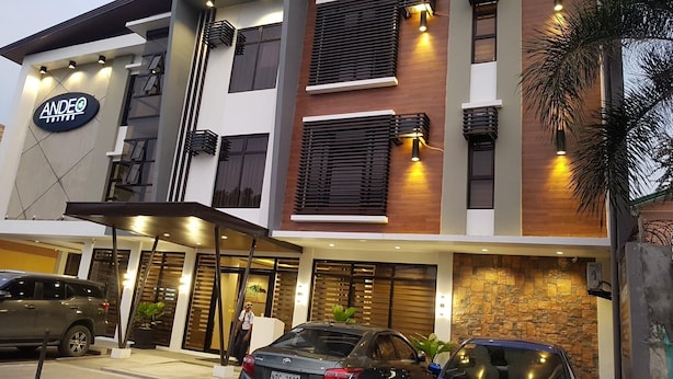 A modern hotel with a sign reading 'ANDEO SUITES,' featuring a two-story structure with a flat roof, large windows, and a stone facade.