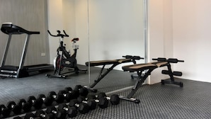 A gym with a treadmill, stationary bike, bench press, and dumbbells.