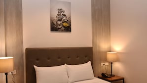 A hotel room with a bed, two bedside lamps, a telephone, and a painting on the wall.
