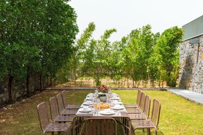 An outdoor dining area with a stone wall, metal chairs, and a table set for a meal. - ELIVAAS Stone Age 4BHK Villa with Pool  (Jalsu)
