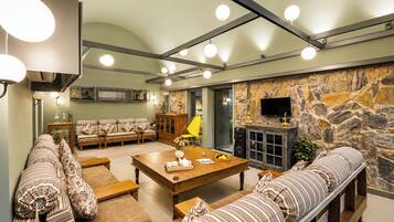 A modern living room with a stone wall, a fireplace, and a television. There are sofas, a coffee table, and a yellow chair.