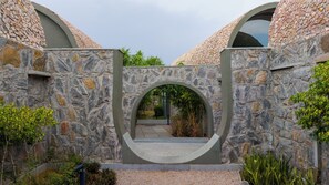 A stone archway leading to a courtyard with a stone wall and greenery. - ELIVAAS Stone Age 4BHK Villa with Pool  (Jalsu)