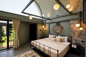 A bedroom with a bed, a stone wall, and a skylight. - ELIVAAS Stone Age 4BHK Villa with Pool  (Jalsu)