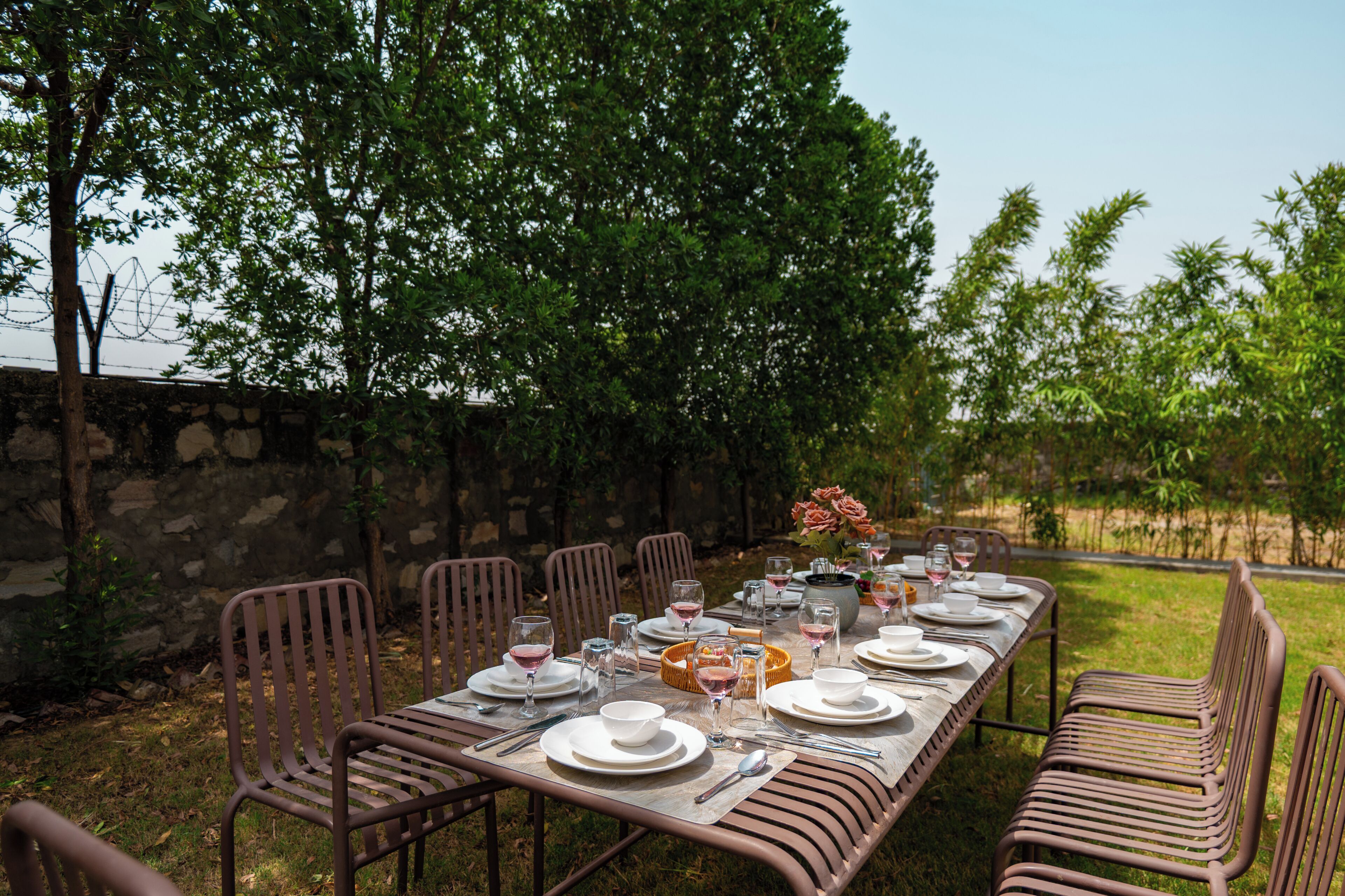Zona pranzo all'aperto con un tavolo lungo apparecchiato per un pasto, circondato da sedie e un muro in pietra.