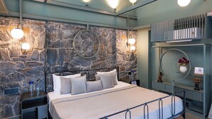 Een moderne slaapkamer met een stenen muur, een bed met veel kussens, nachtkastjes en een ronde spiegel aan de muur.
