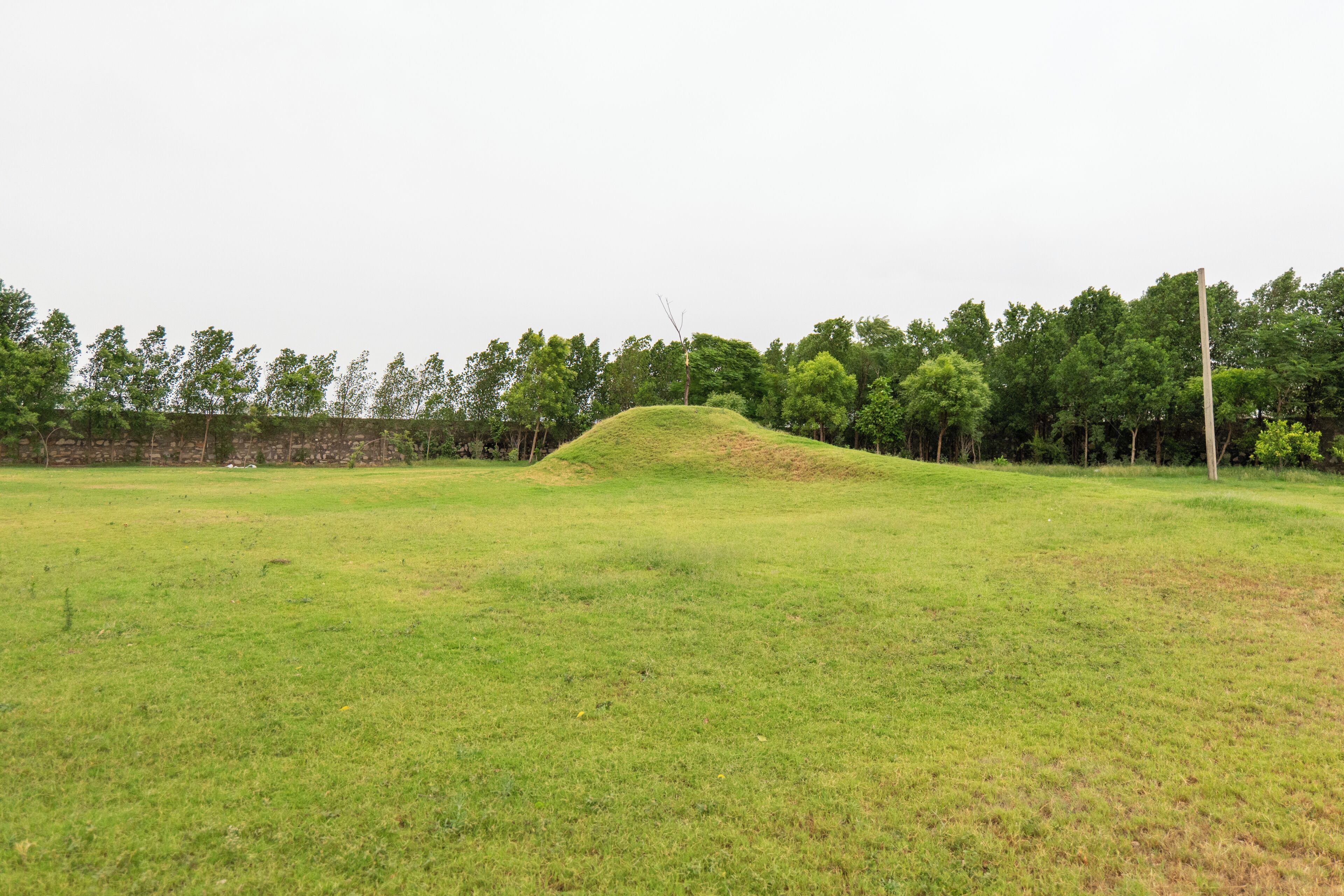 Ein grasbewachsenes Feld mit einem Hügel in der Mitte und einer Steinmauer im Hintergrund.
