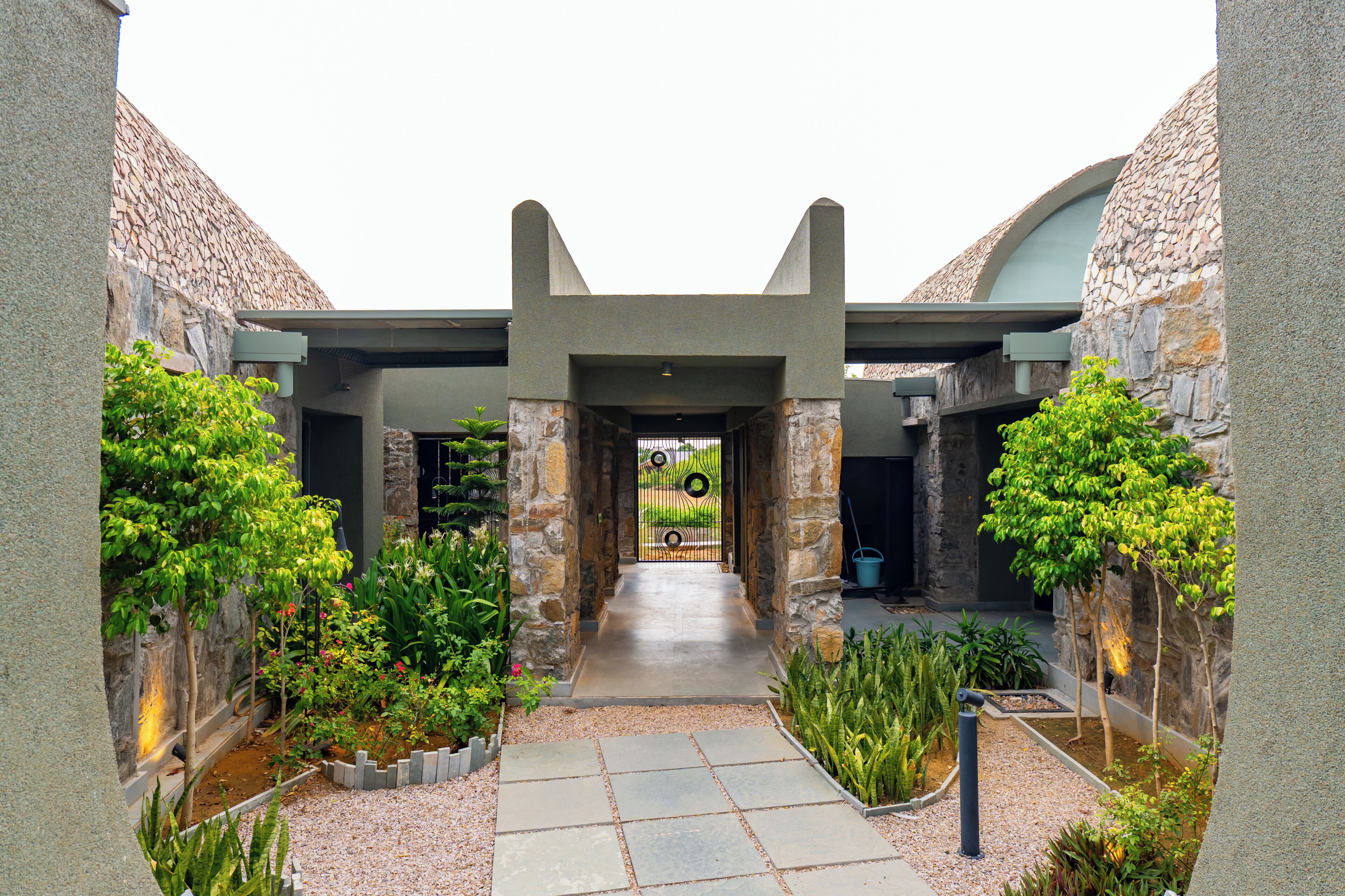 A courtyard with a stone pathway leading to a gate, surrounded by greenery and stone walls.
