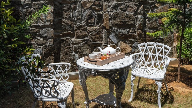 Een stenen muur met een metalen tafel en twee stoelen in een tuin.
