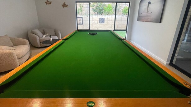 A pool table with a green felt surface, a sofa, and a window with a view of the outside. - Dawesville Family Beach Getaway – Steps from the Sand & Estuary (Dawesville)