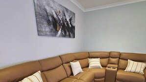 A modern living room with a brown sectional sofa, a gray area rug, and a painting on the wall. - Dawesville Family Beach Getaway – Steps from the Sand & Estuary (Dawesville)