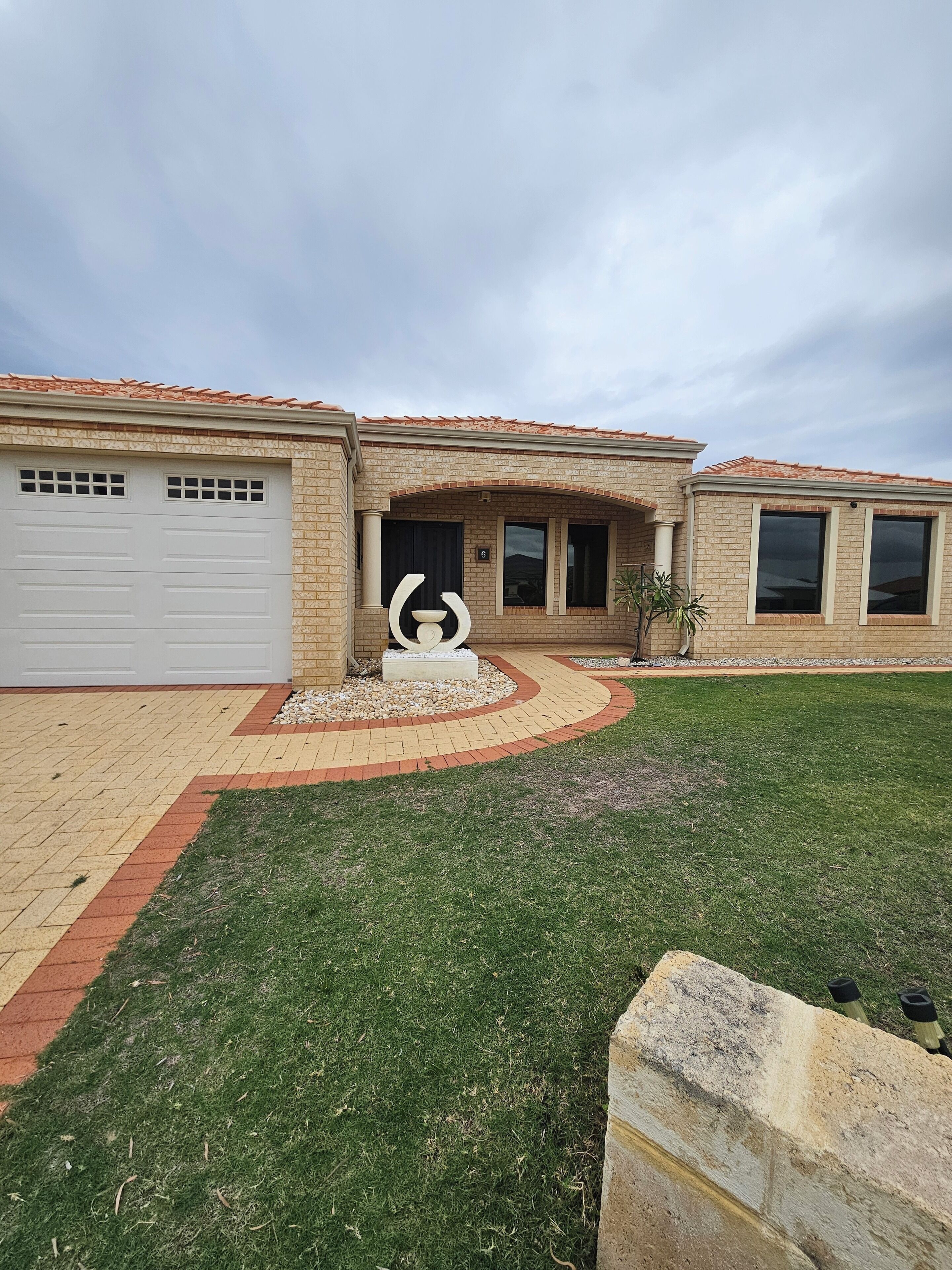 A residential building with a garage, a landscaped front yard, and a decorative sculpture.