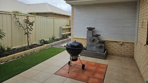 A patio area with a barbecue grill, a small garden with plants, and a brick wall. - Dawesville Family Beach Getaway – Steps from the Sand & Estuary (Dawesville)