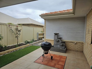 Um espaço de pátio com churrasqueira, um pequeno jardim com plantas e um muro de tijolos.