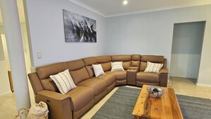 A living room with a brown sectional sofa, a wooden coffee table, a gray area rug, and a ceiling fan. - Dawesville Family Beach Getaway – Steps from the Sand & Estuary (Dawesville)