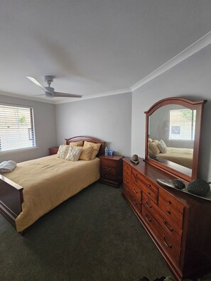 A bedroom with a bed, a dresser, a mirror, a nightstand, and a ceiling fan. - Dawesville Family Beach Getaway – Steps from the Sand & Estuary (Dawesville)