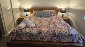 A bedroom with a wooden bed, a ceiling fan, two bedside lamps, and a floral bedspread. - Dawesville Family Beach Getaway – Steps from the Sand & Estuary (Dawesville)