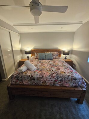 Quarto com cama de madeira, ventilador de teto, duas luminárias de cabeceira e colcha florida.