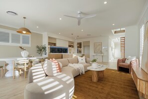 A modern living room with a sofa, coffee table, and a dining area with chairs. - Nordica – Stunning New Build, Bay Views, Steps to Wynnum & Manly Luxury Sleep 10 (Wynnum)