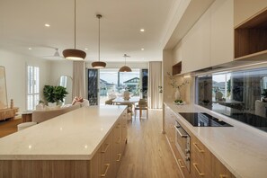 A modern kitchen with a large island, wooden cabinets, and pendant lighting. - Nordica – Stunning New Build, Bay Views, Steps to Wynnum & Manly Luxury Sleep 10 (Wynnum)