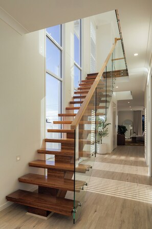 A modern staircase with glass railings and wooden steps leading to an upper floor.